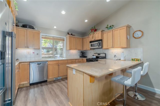 kitchen featuring stainless steel appliances, kitchen peninsula, light hardwood / wood-style floors, vaulted ceiling, and a breakfast bar area