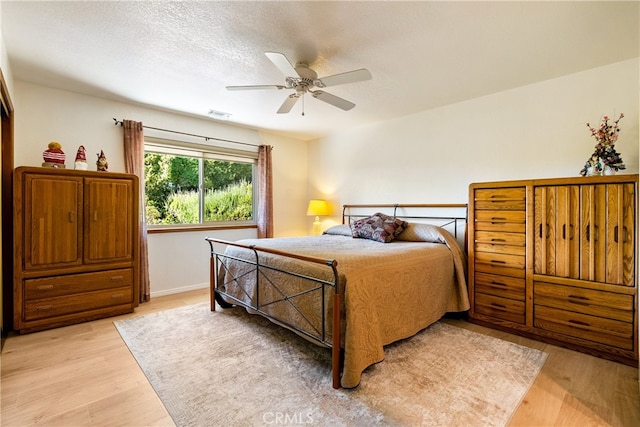 bedroom with light wood-type flooring, ceiling fan, and a textured ceiling