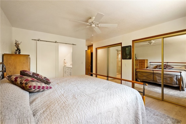 bedroom featuring a barn door, hardwood / wood-style floors, multiple closets, and ceiling fan