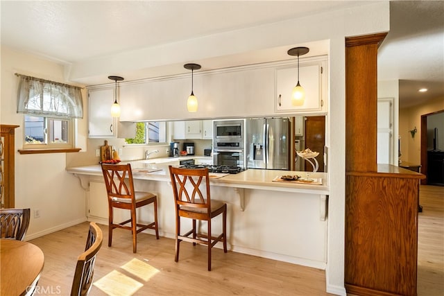 kitchen with white cabinets, kitchen peninsula, appliances with stainless steel finishes, a kitchen breakfast bar, and light wood-type flooring