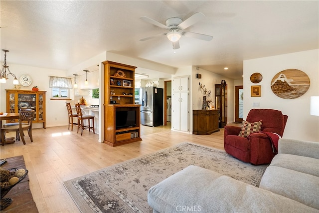 living room featuring ceiling fan with notable chandelier and light hardwood / wood-style flooring