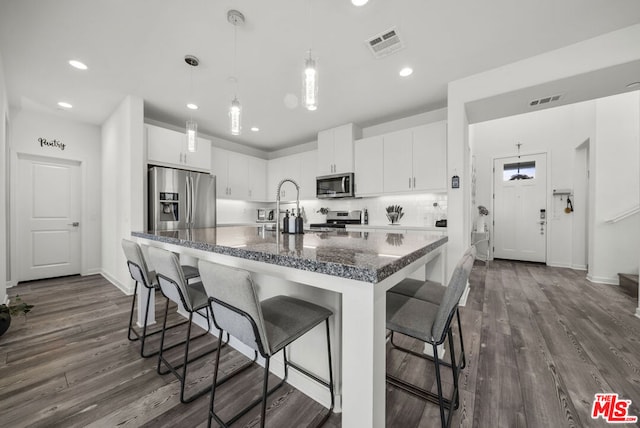 kitchen featuring a kitchen bar, white cabinets, appliances with stainless steel finishes, and dark hardwood / wood-style flooring