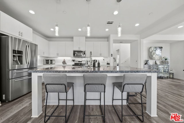 kitchen with dark wood-type flooring, white cabinets, appliances with stainless steel finishes, and a breakfast bar