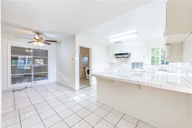 kitchen featuring white cabinets, tile counters, washer / dryer, and kitchen peninsula