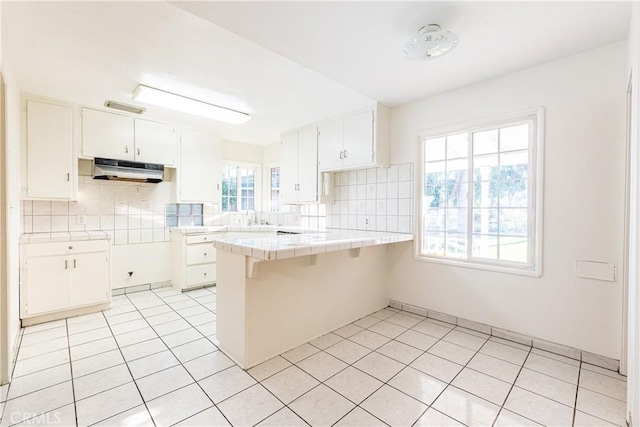 kitchen with kitchen peninsula, tile countertops, white cabinetry, and a wealth of natural light