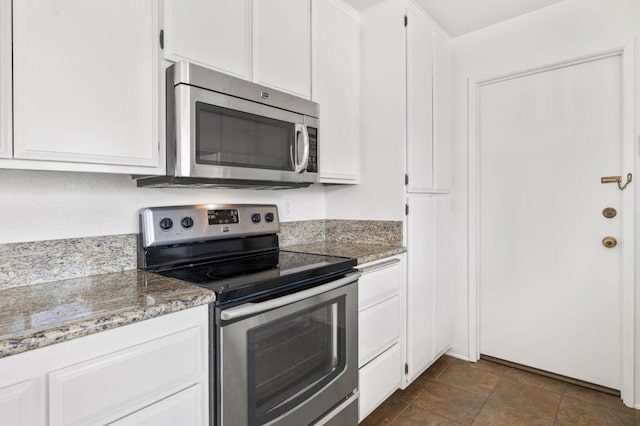 kitchen featuring white cabinets, dark tile patterned flooring, stone countertops, and appliances with stainless steel finishes