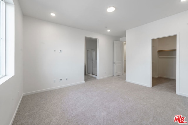 unfurnished bedroom featuring a closet, a walk in closet, and light colored carpet