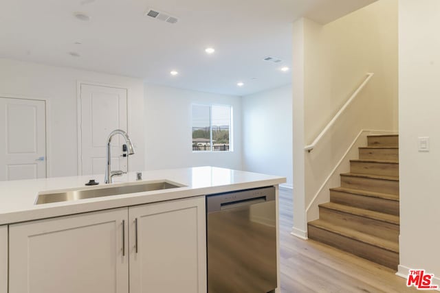 kitchen with stainless steel dishwasher, white cabinets, sink, and light hardwood / wood-style flooring