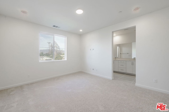 unfurnished bedroom with sink, light carpet, and ensuite bath