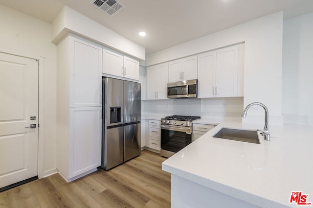 kitchen with kitchen peninsula, stainless steel appliances, white cabinets, light hardwood / wood-style flooring, and sink