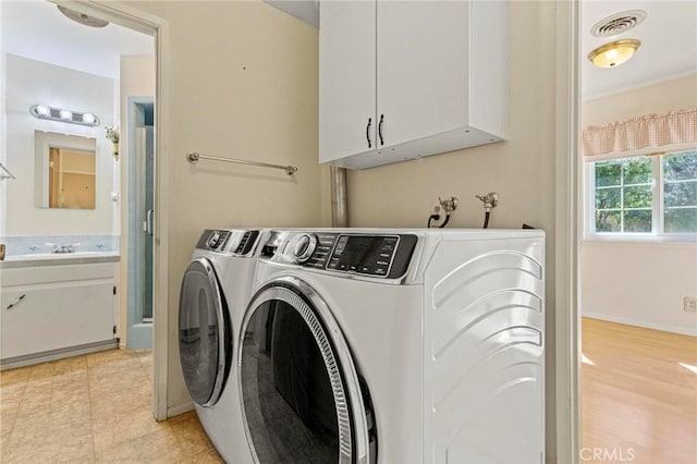 clothes washing area featuring washing machine and dryer, sink, cabinets, and light wood-type flooring