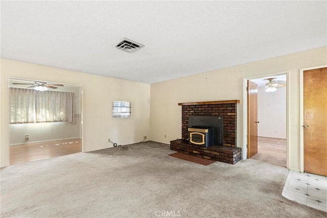 unfurnished living room featuring light colored carpet, a wood stove, and ceiling fan