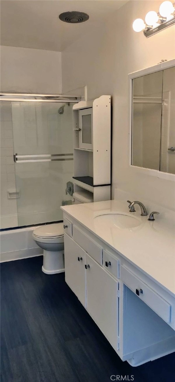 full bathroom with combined bath / shower with glass door, hardwood / wood-style flooring, vanity, and toilet