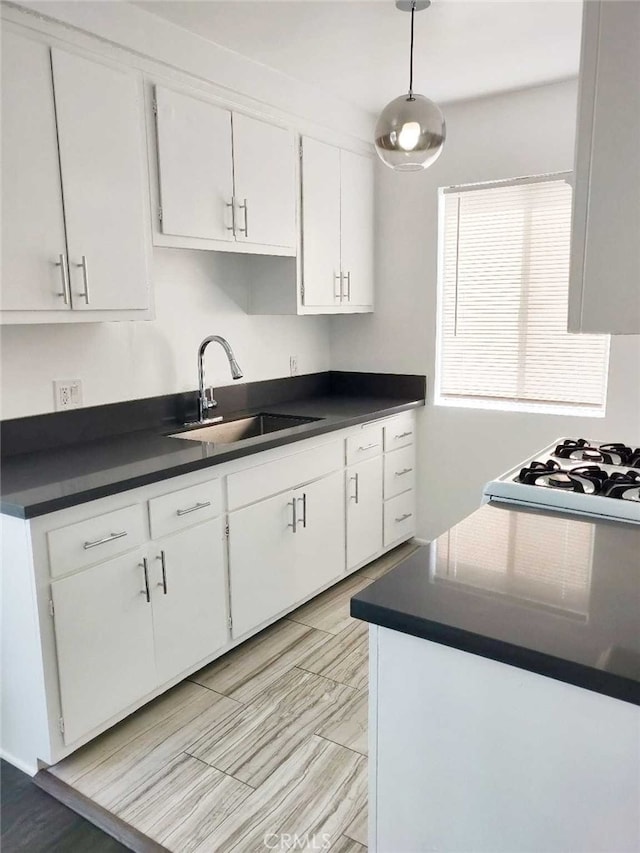 kitchen featuring hanging light fixtures, white cabinetry, sink, and white gas stovetop