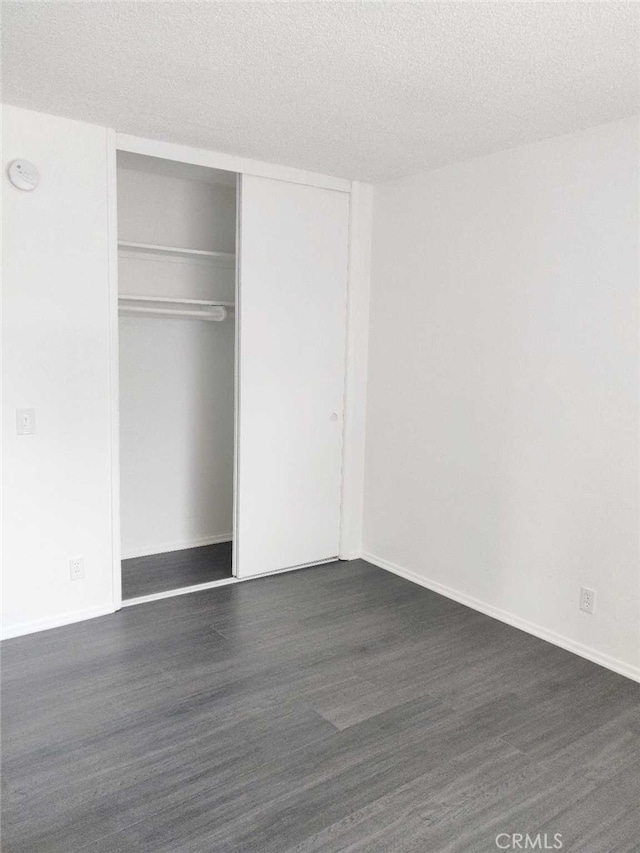 unfurnished bedroom with a textured ceiling, a closet, and dark hardwood / wood-style floors