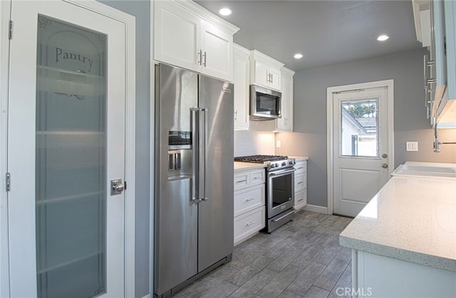 kitchen featuring premium appliances, dark hardwood / wood-style flooring, white cabinetry, and sink