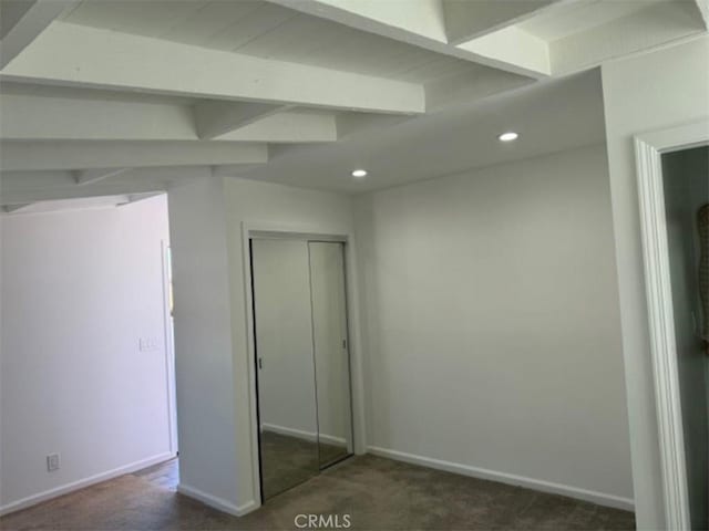 unfurnished bedroom with beam ceiling, a closet, and dark carpet