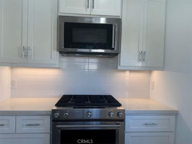 kitchen featuring light stone countertops, backsplash, stainless steel appliances, and white cabinetry