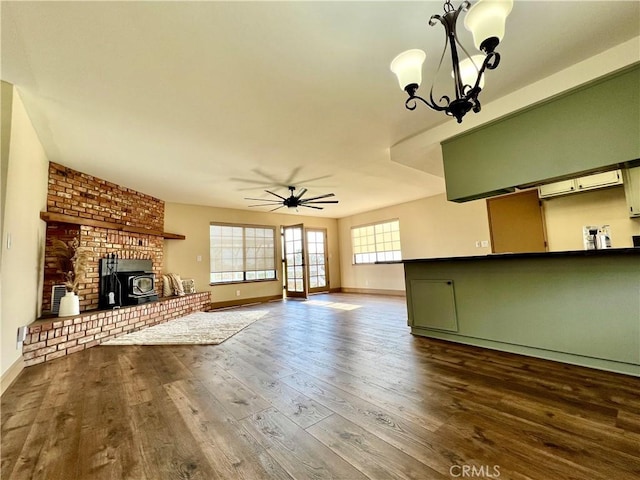 unfurnished living room with ceiling fan with notable chandelier, a wood stove, and wood-type flooring