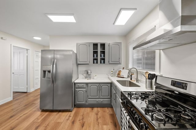 kitchen with wall chimney range hood, gray cabinets, light hardwood / wood-style floors, sink, and stainless steel appliances