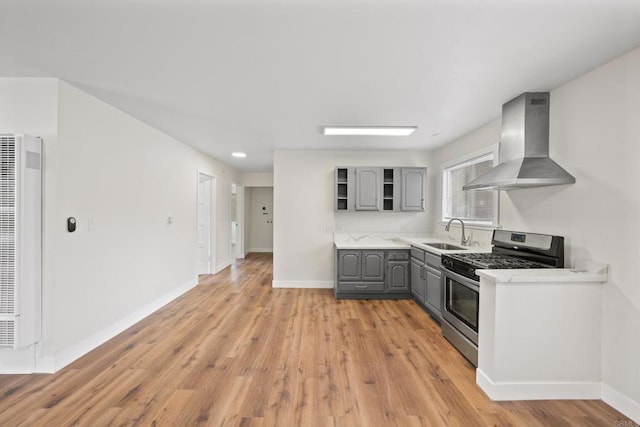 kitchen with sink, gas range, wall chimney exhaust hood, gray cabinets, and light wood-type flooring