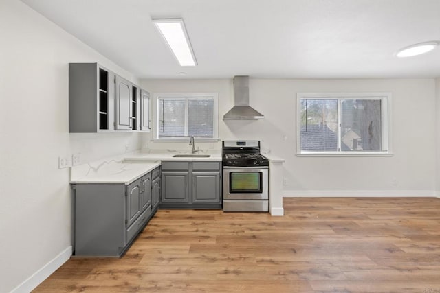 kitchen featuring gray cabinets, wall chimney exhaust hood, gas range, and light hardwood / wood-style flooring