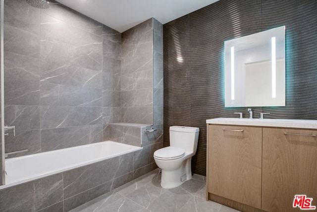 full bathroom featuring vanity, toilet, tiled shower / bath, and tile walls