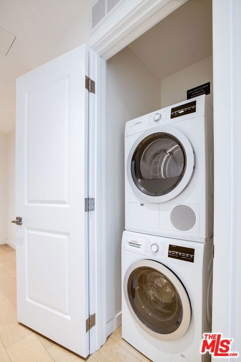 laundry room featuring light wood-type flooring and stacked washer and dryer