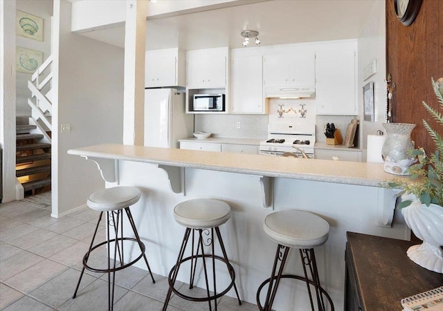 kitchen with tasteful backsplash, white cabinets, white appliances, a kitchen bar, and light tile patterned floors