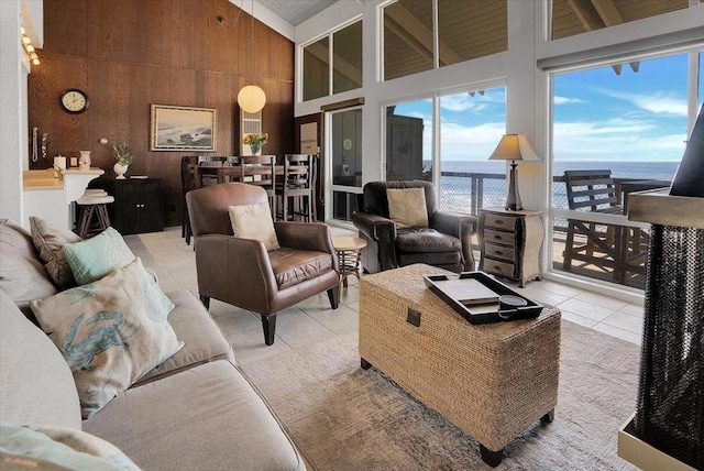 living room featuring wood walls, a water view, light tile patterned flooring, and high vaulted ceiling