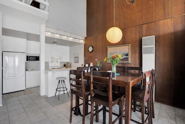 dining room featuring a high ceiling, light tile patterned floors, and wood walls