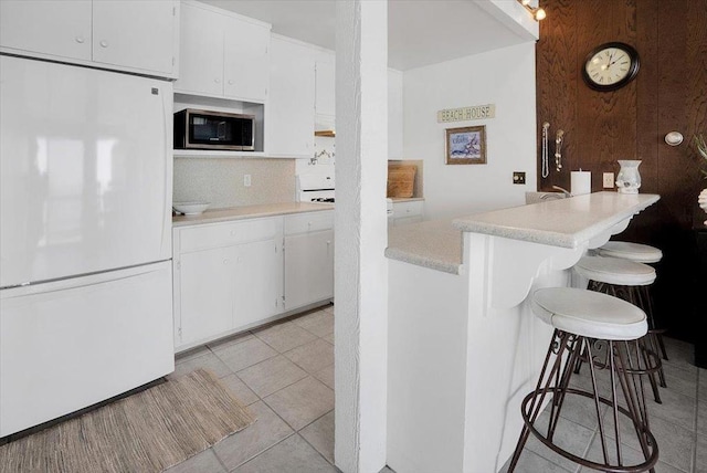 kitchen with a kitchen bar, kitchen peninsula, tasteful backsplash, white refrigerator, and white cabinetry