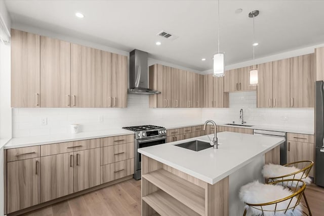 kitchen featuring an island with sink, stainless steel appliances, wall chimney exhaust hood, sink, and light hardwood / wood-style floors