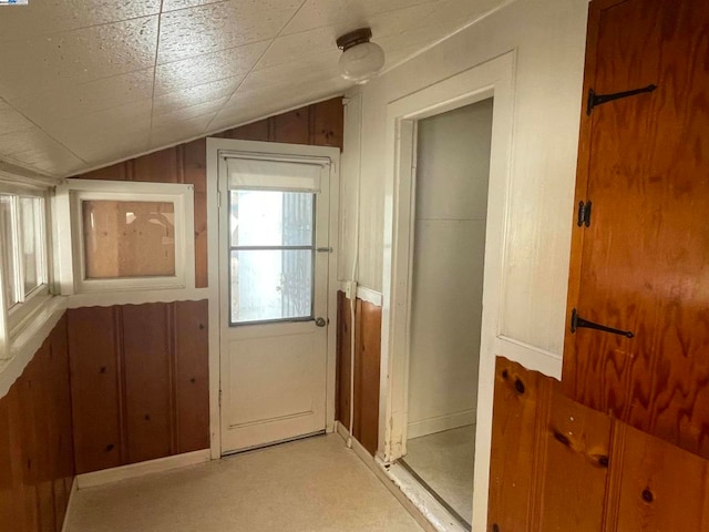 doorway to outside featuring wood walls, vaulted ceiling, and light colored carpet