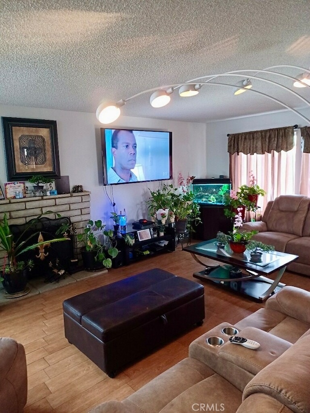 living room with light hardwood / wood-style floors, a textured ceiling, and a brick fireplace