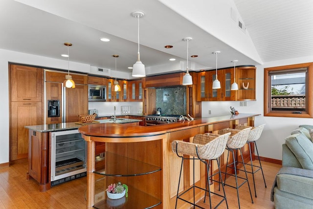 kitchen featuring wine cooler, sink, built in appliances, hanging light fixtures, and light hardwood / wood-style flooring