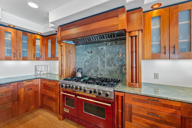 kitchen with stove, light stone counters, light hardwood / wood-style floors, custom range hood, and decorative backsplash