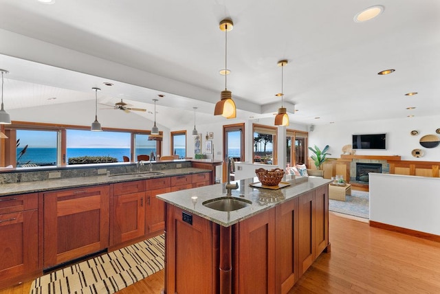 kitchen featuring sink, a water view, hanging light fixtures, an island with sink, and dark stone counters