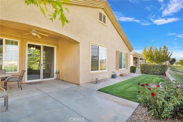 rear view of house with ceiling fan, a patio, and a lawn