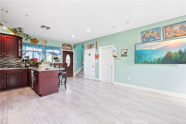 kitchen featuring light stone countertops, tasteful backsplash, light hardwood / wood-style floors, kitchen peninsula, and a kitchen breakfast bar