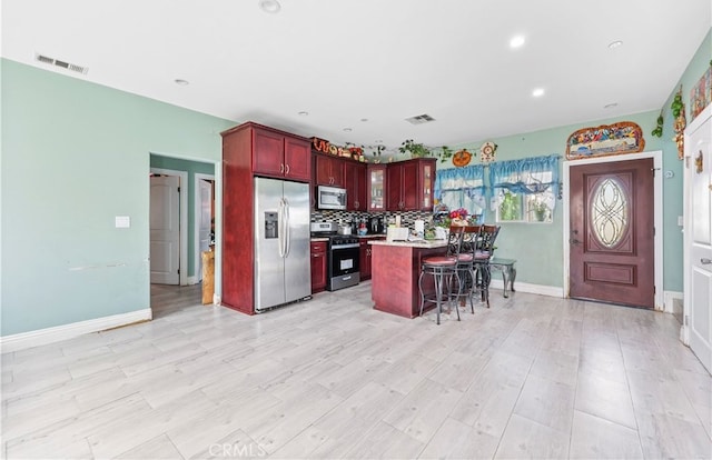 kitchen featuring a kitchen island, stainless steel appliances, tasteful backsplash, light hardwood / wood-style flooring, and a kitchen breakfast bar