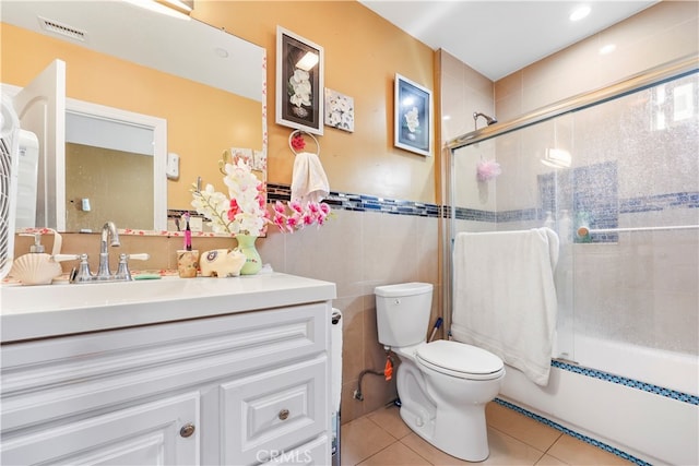 full bathroom with toilet, tile patterned floors, shower / bath combination with glass door, tile walls, and vanity