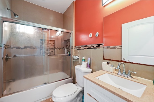 full bathroom with bath / shower combo with glass door, tile walls, vanity, and toilet