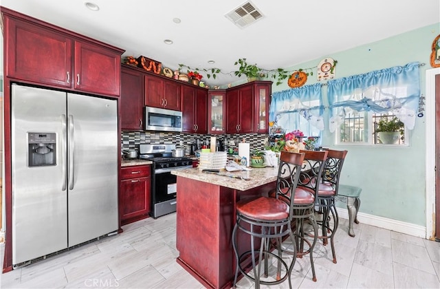 kitchen with stainless steel appliances, a breakfast bar area, tasteful backsplash, and light stone counters