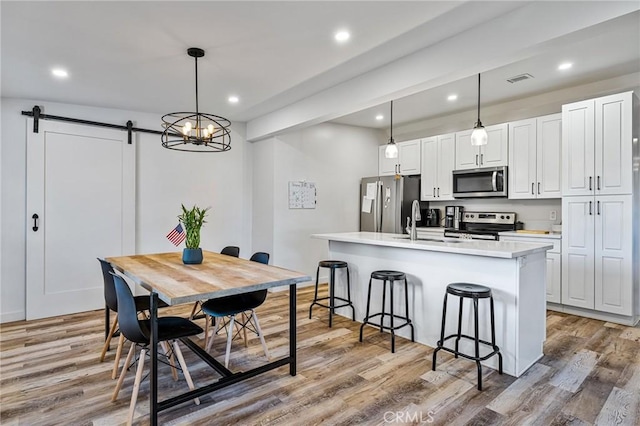 24120 Manzanita St, Menifee, CA 92584 - kitchen with appliances with stainless steel finishes, a barn door, a breakfast bar, light countertops, and an island with sink