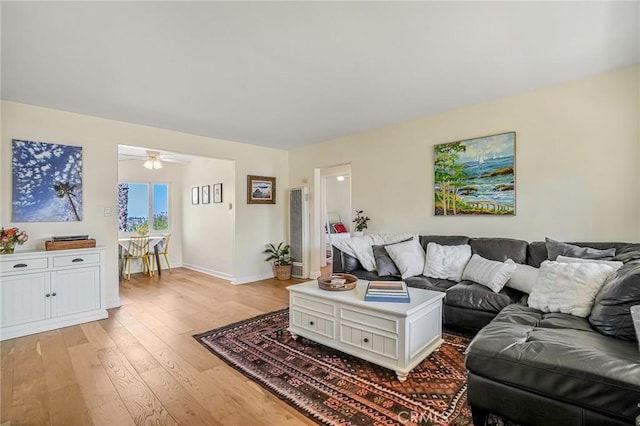 living room featuring a ceiling fan, baseboards, and light wood finished floors