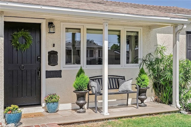 view of exterior entry with roof with shingles and stucco siding