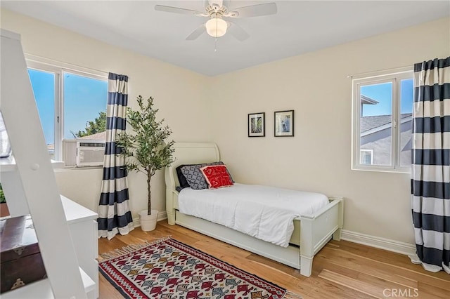 bedroom featuring a ceiling fan, cooling unit, baseboards, and wood finished floors