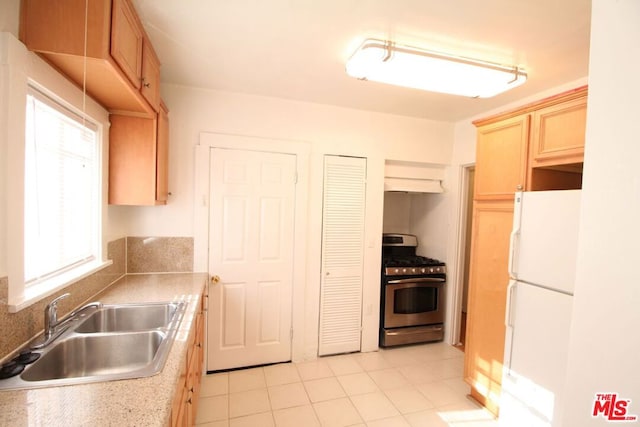 kitchen with sink, light tile patterned flooring, stainless steel range with gas cooktop, white fridge, and light brown cabinetry