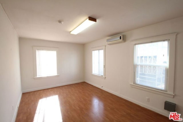 spare room with wood-type flooring, plenty of natural light, and a wall unit AC